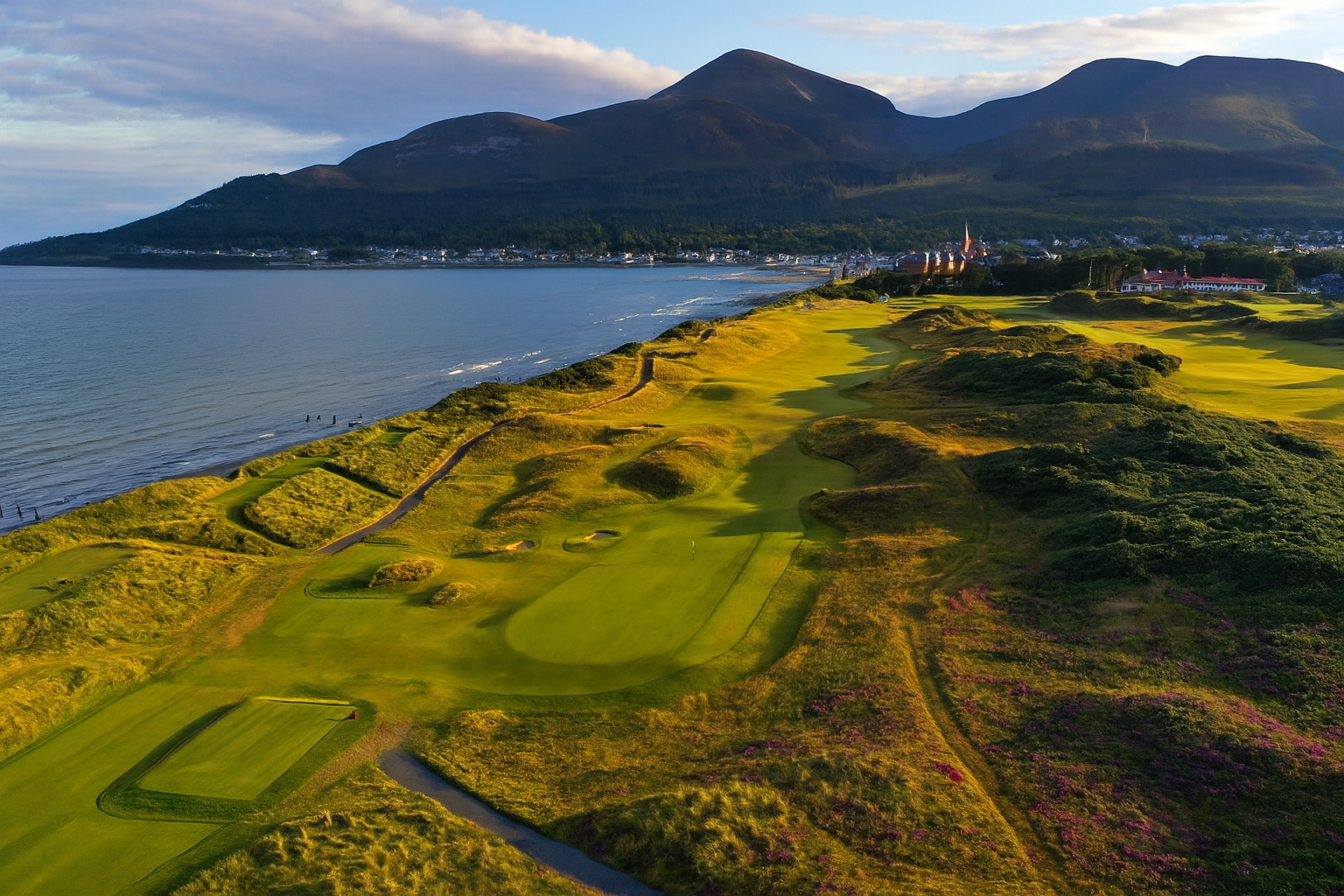 Golf Tours a golf course with a body of water and mountains in the background with Royal County Down Golf Club in the background